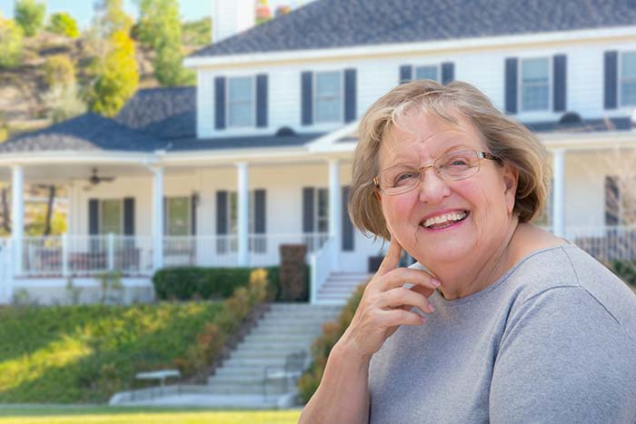 Old woman smiling in front of large home